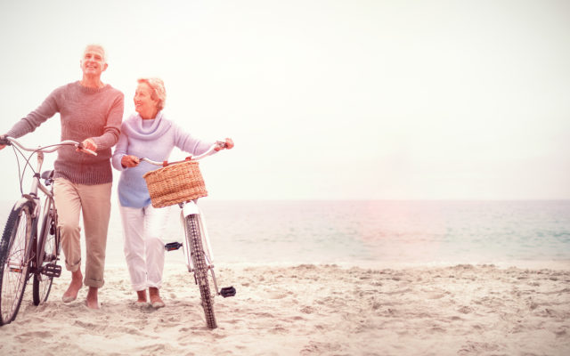 Casal de idosos empurrando bicicletas na praia